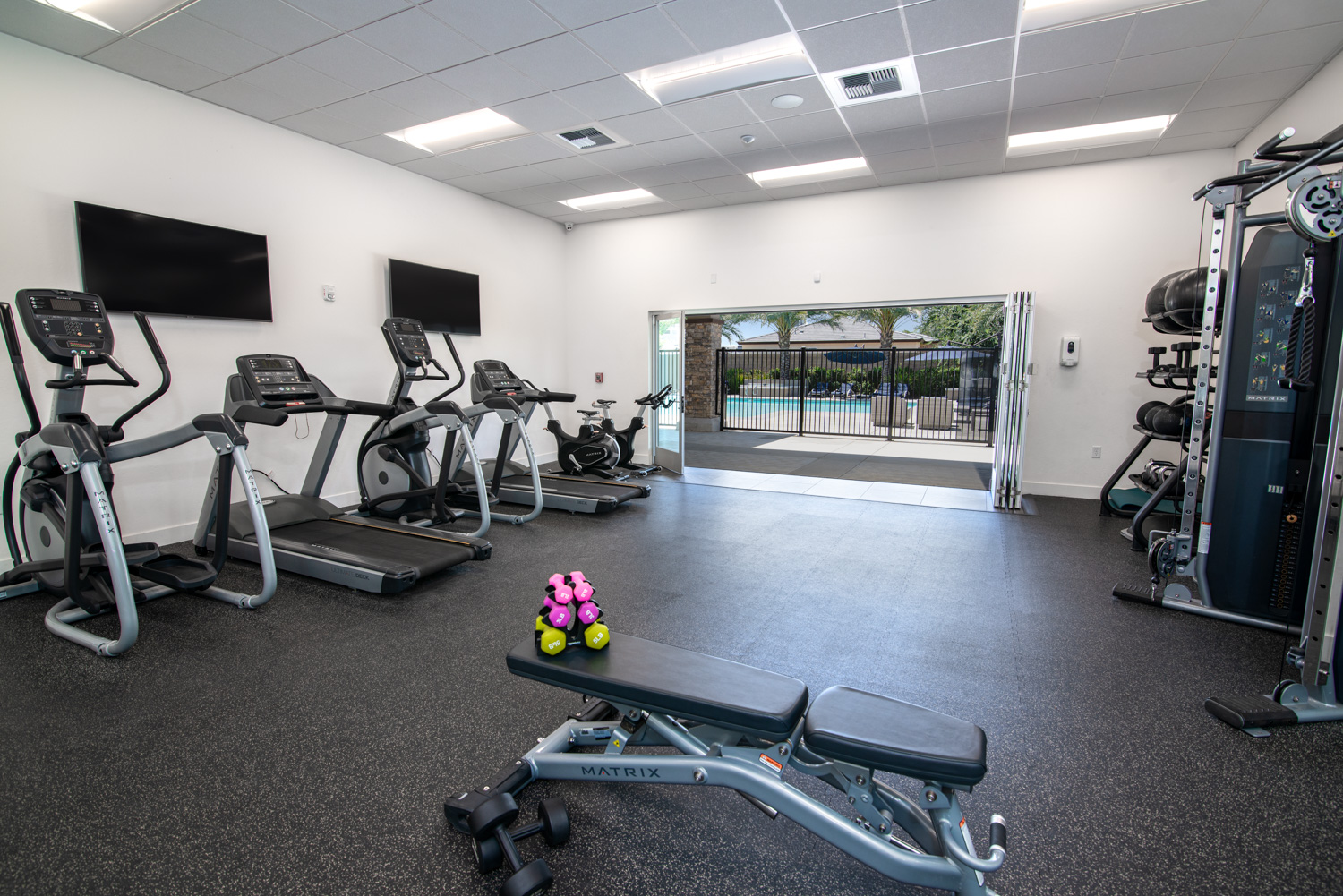 After image of the same fitness area, now vividly showcasing the details of the equipment with correct color balance and natural shadows. The improvements in the photo allow a clear view through the expansive window wall, revealing the scenic outdoors that complement the high-end interior.