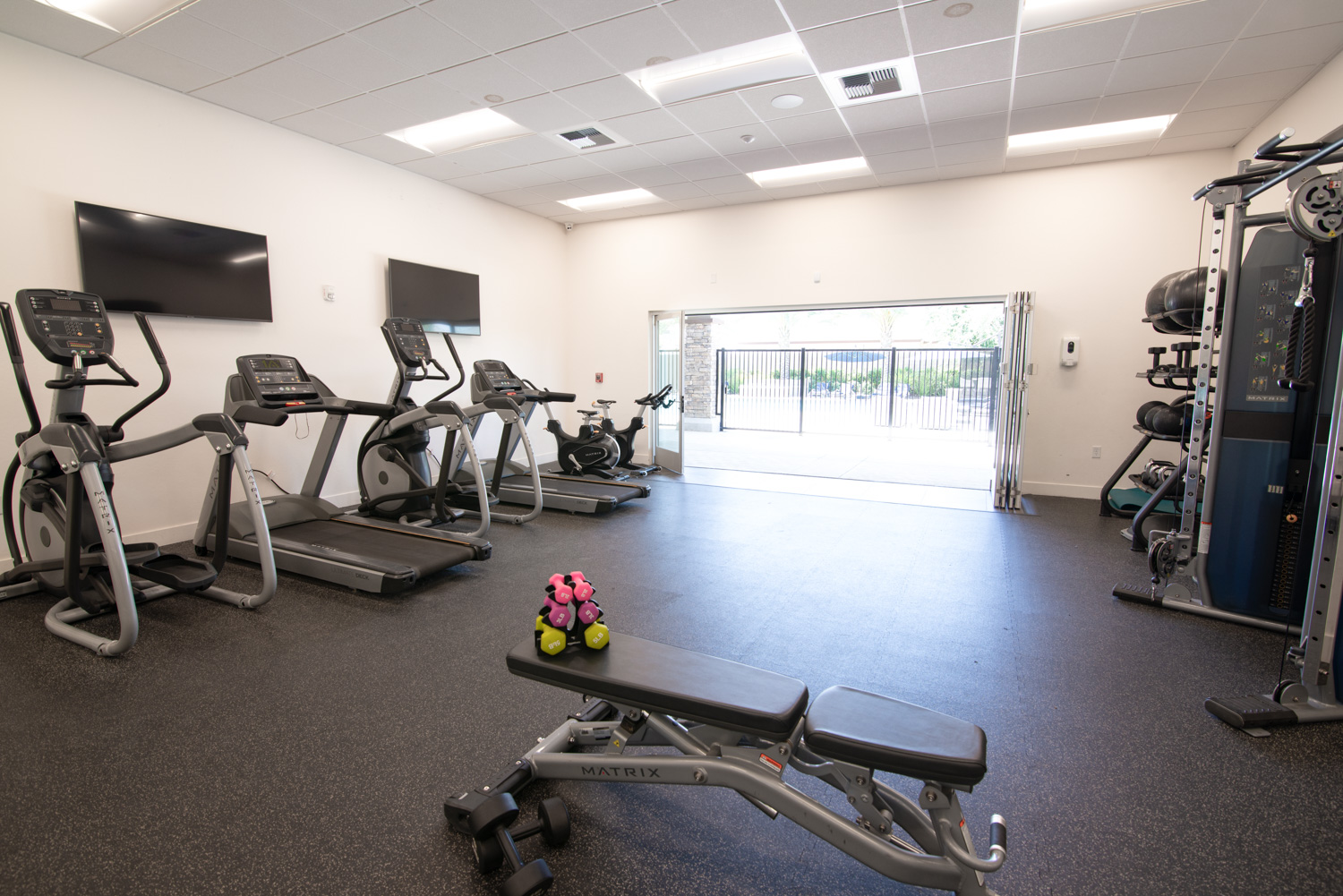 Before image of a high-end fitness center equipped with top-notch workout machines. Although the space is designed for an optimal exercise experience, the photo&#039;s colors are not accurately represented, and the view from the expansive window wall is obscured, diminishing the visual appeal of the setting.